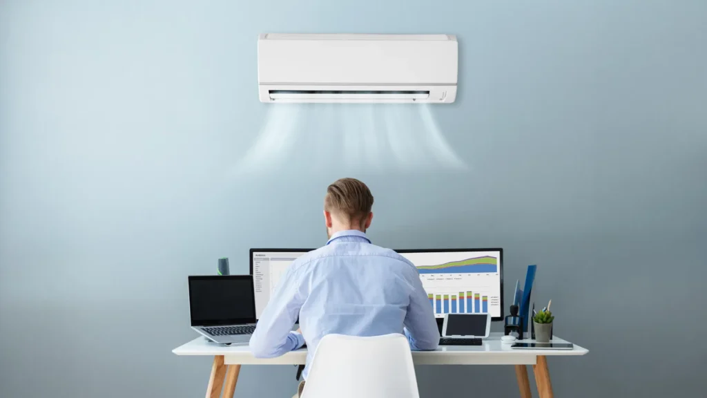 mężczyzna podczas pracy a nad nim klimatyzator naścienny
